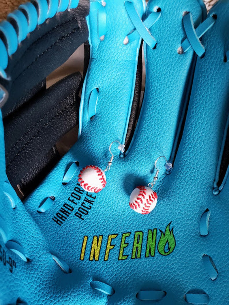 May include: A pair of baseball-themed earrings with red stitching on a white background. The earrings are hanging from a blue baseball glove with the word "INFERNO" printed on it.