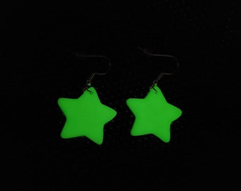 May include: A pair of green star-shaped earrings with silver hooks. The stars are glowing in the dark.