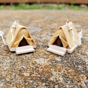 May include: A pair of brown and white tent-shaped earrings with silver hooks. The tents have a brown flap and a white base.