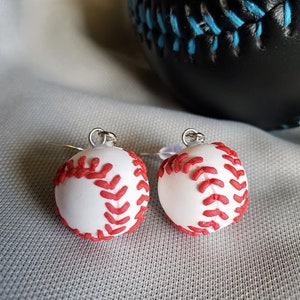 May include: A pair of silver earrings with white baseball charms. The baseball charms have red stitching.