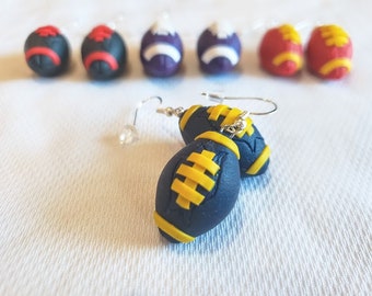 May include: A pair of dangle earrings featuring a black and yellow football design. The footballs are made of polymer clay and have a realistic look.