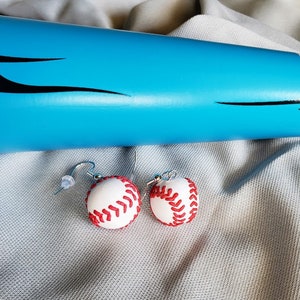 May include: A pair of baseball-themed earrings with white and red baseballs hanging from silver hooks.