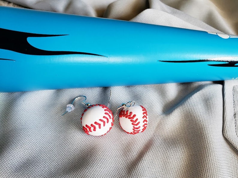 May include: A pair of baseball-themed earrings with white and red baseballs hanging from silver hooks.
