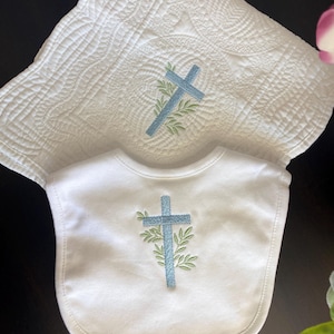 K&ouml;nnte beinhalten: Wei&szlig;es Baby-L&auml;tzchen- und Decken-Set. Das L&auml;tzchen und die Decke haben ein hellblaues Kreuzdesign mit gr&uuml;nen Bl&auml;ttern. Die Decke hat ein gestepptes Muster.