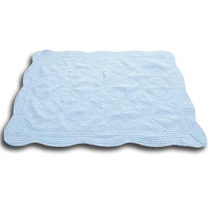 K&ouml;nnte beinhalten: Eine hellblaue, gesteppte Decke mit einem gewellten Rand. Die Decke hat ein sich wiederholendes Muster aus ovalen Formen mit detaillierten N&auml;hten. Das Design ist symmetrisch und die Decke ist wahrscheinlich aus einem weichen Stoff.