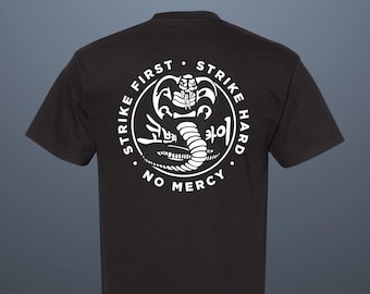 Könnte beinhalten: Schwarzes T-Shirt mit einem weißen Kreis-Motiv, das eine Kobra und den Text "Strike First Strike Hard No Mercy" zeigt.