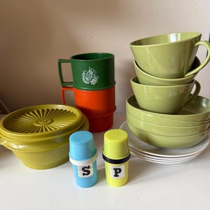 May include: A selection of retro kitchen items in shades of green, orange, and yellow. The set includes mugs, bowls, plates, and salt and pepper shakers. The salt and pepper shakers are labelled with the letters "S" and "P".