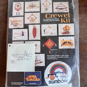 Puede incluir: Un kit de bordado Crewel con temática del suroeste en una bolsa de plástico transparente. El kit presenta varios diseños, incluyendo cactus, una rueda de carro y un hombre arcoíris. El texto "Crewel Kit" y "sunbow" son visibles. El kit incluye todos los materiales, excepto el marco.