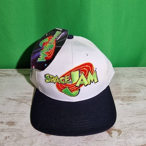 May include: White baseball cap with a black brim. The front of the cap features a green, red, and yellow embroidered Space Jam logo.