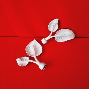 Peut inclure: Deux embouts en métal blanc avec des motifs de feuilles. Les embouts sont sur un fond rouge.