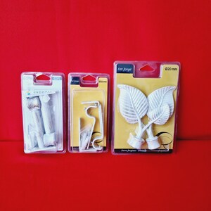 Peut inclure: Trois embouts de rideau en métal blanc. Les embouts sont en forme de feuilles. Les emballages sont étiquetés avec le texte "Fer Forge" et "Ø20 mm".