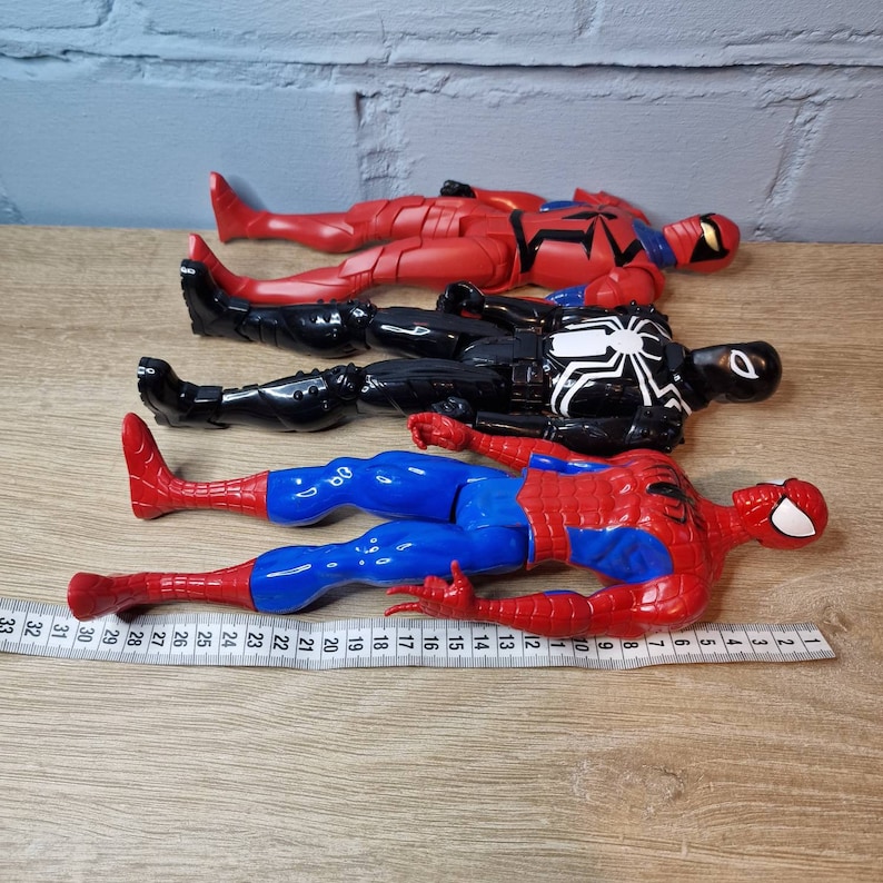 Pu&ograve; includere: Quattro action figure di supereroi, tra cui Spider-Man, Venom e due versioni di Spider-Man in costume rosso e nero. Le figure sono posizionate su una superficie di legno con un metro a nastro.