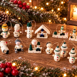 Puede incluir: Una colección de pequeños adornos de madera pintados a mano con forma de muñeco de nieve, que presentan varios diseños, incluyendo figuras con sombreros, bufandas y accesorios en miniatura. Cada adorno incluye un cordel para colgar.
