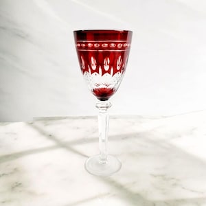 Op de afbeelding: Een helder wijnglas met een rode voet en een ingewikkeld gesneden glasontwerp. Het glas heeft een lange steel en een ronde kom.