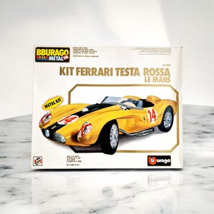Könnte beinhalten: Ein Die-Cast-Metallbausatz eines gelben Ferrari Testa Rossa Le Mans Rennwagens. Die Box zeigt das Auto mit der Nummer 14, schwarzen Rennstreifen und dem Burago-Logo. Auf der Box stehen auch die Wörter "Metal Kit" und "Die-Cast Metal".