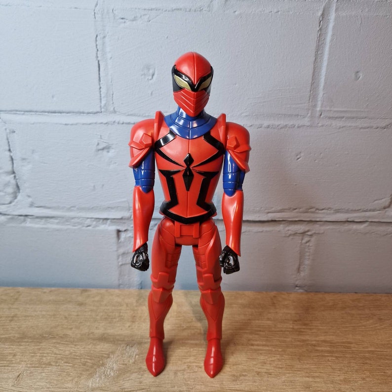 Pu&ograve; includere: Figurina d'azione rossa e blu di un supereroe con casco e armatura. La figura ha un simbolo di ragno sul petto.