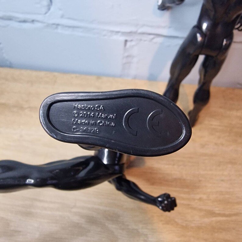 May include: Close-up of the bottom of a black plastic action figure. The figure's foot is visible. The bottom of the foot has the following text: Hasbro GA &copy; 2014 Marvel Made in China C-20325 CE