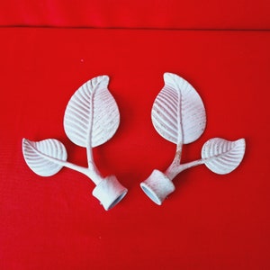 Puede incluir: Dos remates de metal blanco en forma de hoja con un acabado decorativo desgastado. Cada remate tiene tres hojas y una base redonda.