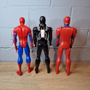 Pu&ograve; includere: Tre action figure di supereroi. La figura a sinistra &egrave; rossa e blu con un logo a forma di ragno sul petto. La figura al centro &egrave; nera con un logo a forma di ragno bianco sul petto. La figura a destra &egrave; rossa con una maschera nera.