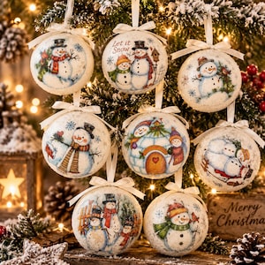 Puede incluir: Un conjunto de ocho adornos navideños redondos de color blanco roto con ilustraciones de muñecos de nieve en diversas escenas invernales. Cada adorno tiene un lazo de cinta blanca y muestra motivos festivos como muñecos de nieve e iglús.
