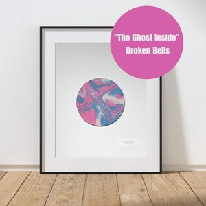 May include: Framed art print featuring a circular design with pink, blue, and white swirls. The artwork is set against a white background within a black frame. A pink circle with the text "The Ghost Inside" and "Broken Bells" is in the upper right corner.