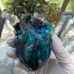 May include: A blue and green resin heart with air bubbles trapped inside. The heart is translucent and has a glossy finish.