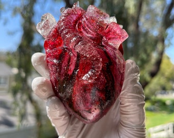 May include: A glass heart sculpture with a red and clear color scheme. The heart is detailed with veins and has a glossy finish.