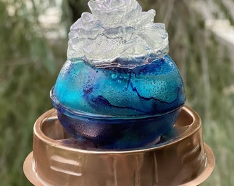 May include: A blue and white glass sphere with a white flower-shaped top, sitting on a copper-colored metal base.