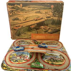 May include: Vintage tin toy race track set with a bridge and three cars. The track is painted with a colorful scene of a highway and a viaduct. The box is also included and features a similar scene.