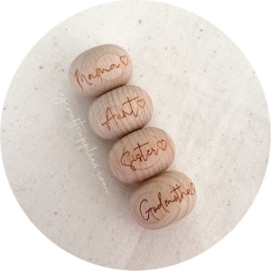 May include: Four wooden engraved ornaments with the words "Momma", "Aunt", "Sister", and "Godmother" on them. Each ornament has a small heart symbol next to the word.