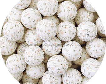 May include: A close-up of a collection of white silicone beads with a floral pattern. The beads are round and have a smooth surface. The floral pattern is in shades of pink and green.