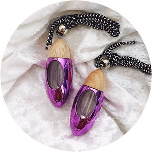 May include: Two purple metallic car air fresheners with wooden tops and clear glass inserts. The fresheners are hanging from black and white cords.