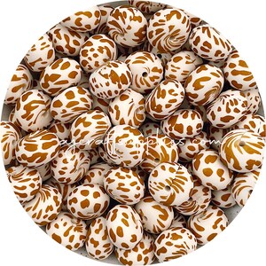 以下が含まれることがあります： ヒョウ柄のブラウンとホワイトのシリコンビーズのセット。ビーズは楕円形で、中央に穴が開いています。