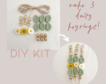 May include: DIY kit for making three daisy keyrings. Contains gold-coloured clasps, beads, green leaf-shaped charms, daisy flower charms, and twine. The image text says "DIY KIT" and "make 3 daisy keyrings!"