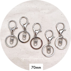 May include: Five silver keyrings with a 70mm diameter ring and a swivel clasp. The keyrings are arranged in a circle on a white fabric background.