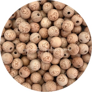 May include: A large group of wooden beads with a koala bear design. The beads are light brown and have a hole in the centre for stringing.