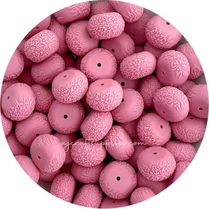 May include: A large group of pink silicone beads with a floral design. The beads are all the same size and shape, and they are arranged in a random pattern.