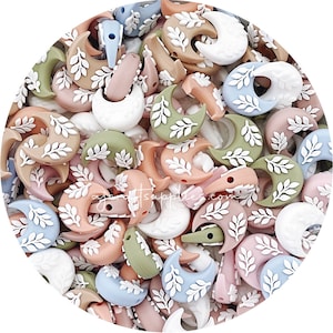May include: A collection of silicone beads in various pastel colours, each bead is shaped like a crescent moon with a white leaf design.