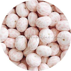 以下が含まれることがあります： ヒョウ柄のピンクと白のシリコンビーズの山をクローズアップした写真。ビーズは丸く、中央に穴が開いています。