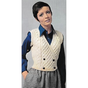 May include: A white knitted vest with a V-neck and double breasted buttons. The vest has a cable knit pattern and is worn over a blue button-down shirt.