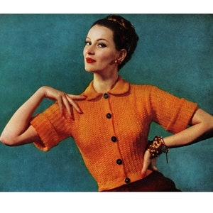 May include: A woman wearing a bright orange knitted cardigan with a collared neckline and button closure. The cardigan has short sleeves and a textured knit pattern. The woman is standing against a teal background.