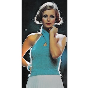 Puede incluir: Una mujer con un top azul de halter con un diseño cruzado y una falda blanca. El top tiene una abertura de ojo de cerradura en la parte delantera. La mujer tiene el pelo rubio corto y lleva una pulsera en la muñeca. El fondo es negro.
