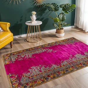 May include: A rectangular rug with a bright fuchsia central design and an ornate border. The border incorporates grey, gold, and floral motifs. The rug's design has a contemporary feel, suitable for living rooms or bedrooms.
