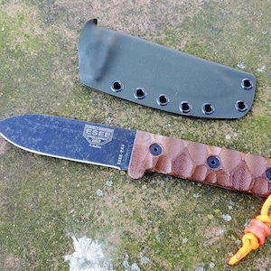 May include: A black ESEE-PK4 fixed blade knife with a brown handle and a green sheath. The knife has a lanyard with an orange and yellow cord. The blade has the ESEE logo.