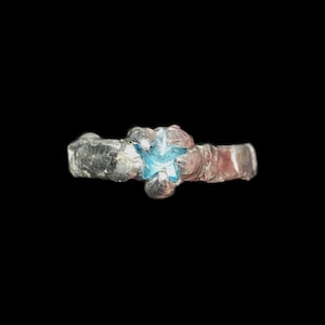 May include: A silver ring with a blue star-shaped gemstone.