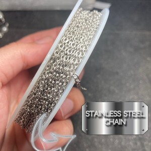 May include: A spool of stainless steel chain. The chain is silver and has a small link design. The text "STAINLESS STEEL CHAIN" is displayed on a metal plate.