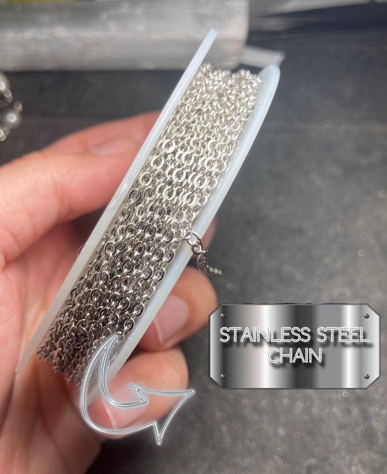 May include: A spool of stainless steel chain. The chain is silver and has a small link design. The text "STAINLESS STEEL CHAIN" is displayed on a metal plate.