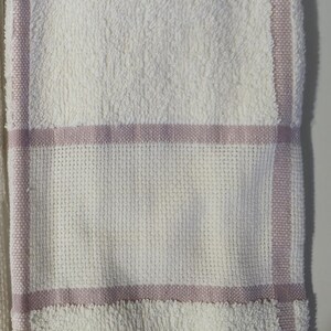 May include: White bath towel with a textured surface and a woven section with a lavender stripe. The towel has a fringe at the bottom edge. A simple and elegant design for the bathroom.