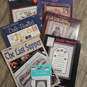 May include: A collection of cross-stitch pattern booklets, including designs from Bucilla, Alma Lynne, and Dale Burdett. The booklets feature religious themes, such as Noah's Ark, The Last Supper, and Cathedral Impressions. The color palette includes blues, reds, and browns.