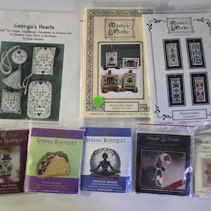May include: A collection of cross-stitch and needlework kits, including designs for Christmas, autumn, and spring. The kits feature various patterns, such as a taco, a candy cane, and geometric designs. The kits are packaged in clear plastic.